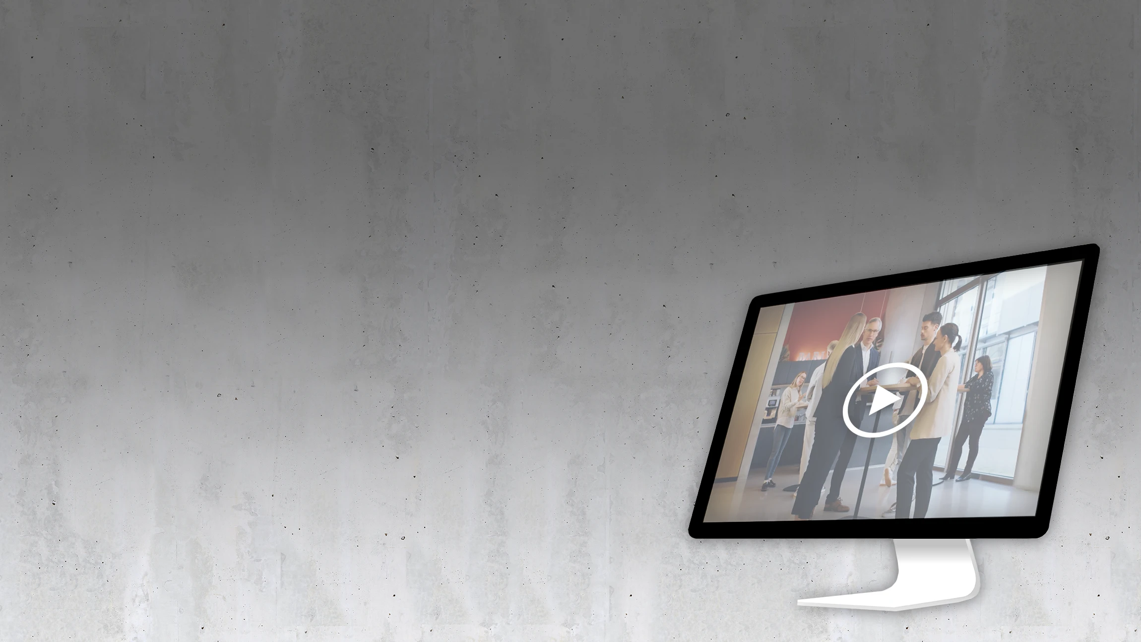 A computer monitor displays a paused video of people in business attire having a conversation in an office setting. The background is a plain, grey concrete wall.
