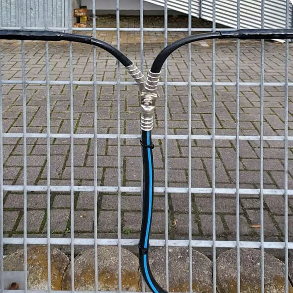 Three cables are joined together and wrapped with tape at a junction, running vertically against a metal fence with a brick pavement in the background.